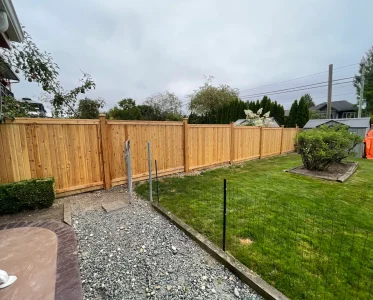 A tall wooden fence in a well-manicured backyard with a grassy lawn and trees.