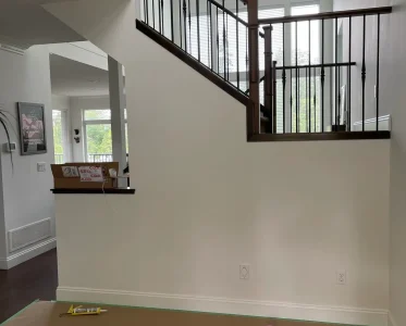 Staircase in a house under renovation with a white wall and brown stairs.