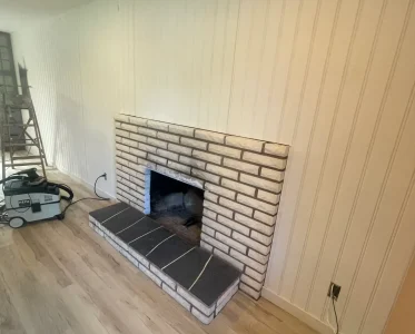 Empty brick fireplace in a clean living room with a bench and vacuum cleaner.